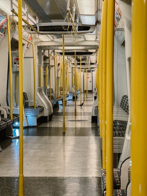 Interior view of a public train carriage in Croydon, featuring rows of patterned fabric-upholstered seats on both sides of a central aisle with a smooth, clean floor. Bright yellow vertical poles and handrails are evenly spaced along the aisle, providing support for standing passengers. Overhead handles and lighting fixtures are visible, contributing to a well-lit environment. The surfaces appear spotless, indicating recent cleaning and maintenance by Carpet Cleaners Croydon, ensuring hygiene and safety for commuters at East Croydon station. The image emphasizes the importance of surface cleaning and sanitisation within public transportation settings to maintain cleanliness and hygiene standards.